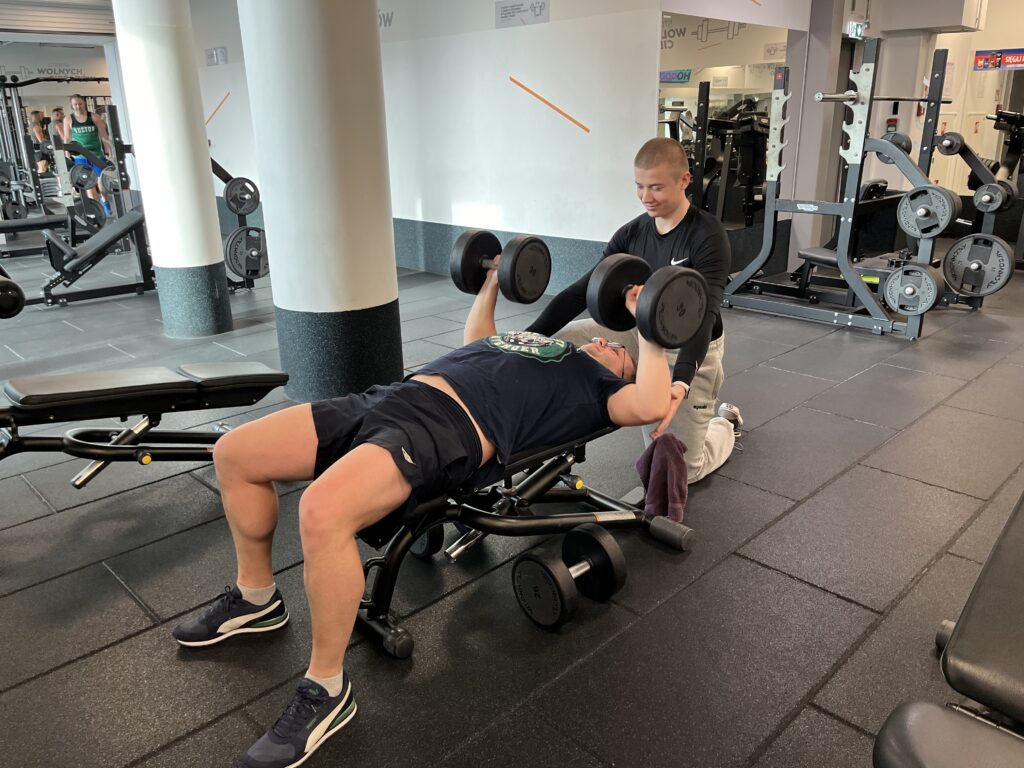 Trening personalny z Adrianem Wyszomirskim w CityFit Wiatraczna – mężczyzna po 30 roku życia wykonuje wyciskanie hantli w programie Redukcja PRO | trener personalny Warszawa Praga-Południe